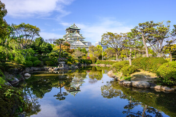 Osaka Castle, a 16th century masterpiece, is mirrored in a calm pond within its expansive gardens. The castles imposing structure contrasts beautifully with the tranquil surrounding landscape.