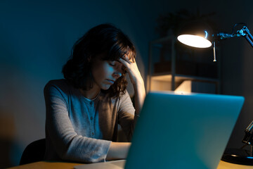 Tired woman working late at night using laptop at home office having headache.