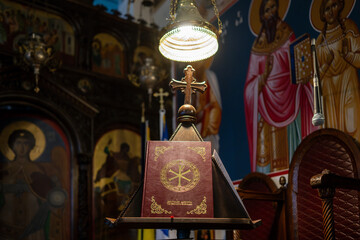 , Deutschland, 28.12.2024,  Eine reich verzierte Bibel mit einem Kreuz, umgeben von Ikonen, in einer orthodoxen Kirche. Stimmungsvoll beleuchtet und detailreich.