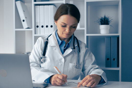 A highly focused and dedicated female doctor is diligently writing notes in her medical office, demonstrating her commitment to patient care and professional collaboration in the healthcare field