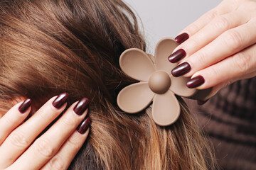 Hair clip in the shape of a flower. Brunette styling her hair with a casual updo. Everyday hairstyle with pinned hair creating an elegant and simple look. Hairstyle modeling background.