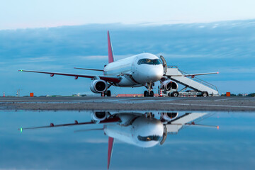 Modern passenger plane with stairway reflected in a puddle at the airport