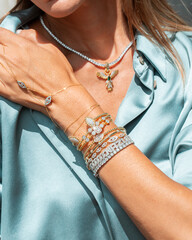 A stylish woman adorned with layered gold and diamond jewelry, 
including necklaces, bracelets, rings.