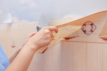 removing wallpaper from the wall with a spatula, the process of updating the wall of nursery room....