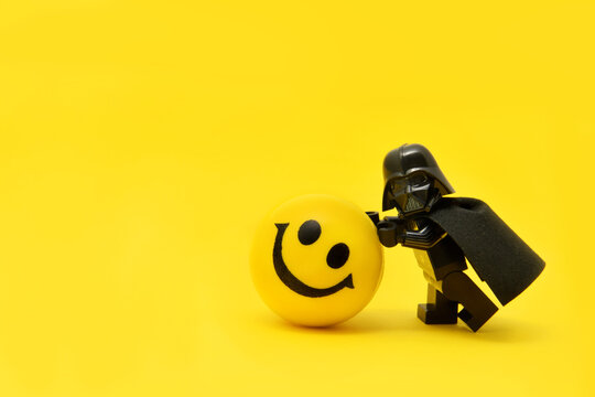 Lego minifigure of Darth Vader or Star Wars evil chef is walking yellow smily face ball isolated on yellow. Editorial illustrative image to stop war. Exclusive.