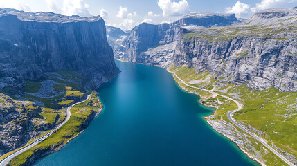 An aerial shot of a bright blue fjord surrounded by tall cliffs and green grass. Two roads flank the water, curving to follow the landscape.