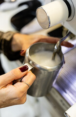 Close-up of woman's hands holding milk pitcher under coffee machine steam wand