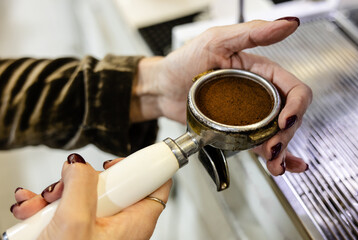 Close-up of woman's hands holding a portafilter filled with ground coffee