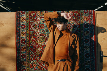 Stylish young man posing against a vibrant, patterned rug background, showcasing contemporary...