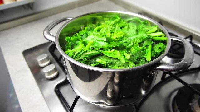Turnip greens are being boiled in a stainless steel pot on a gas stove following the traditional recipe of orecchiette con le cime di rape, an italian traditional dish