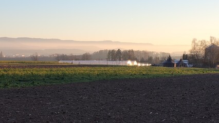 Beautiful morning scenery showing a farm and the mountain ridges of the Swabian Alb in the background. Golden sunlight illuminates the fog in front of the mountains.