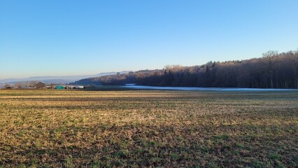 A farmer's field that is partly covered with snow in the background. At the horizon there are the mountain ridges of the Swabian Alb, Germany.