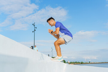Man performs an intense workout on a ledge by the waterfront under a clear blue sky