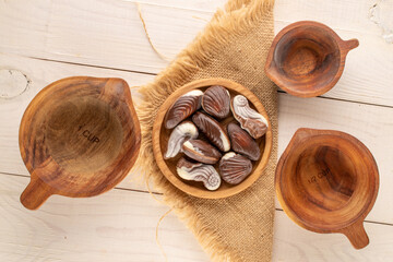 How many chocolate candies with ceramic and wooden utensils on a wooden table, close-up, top view.