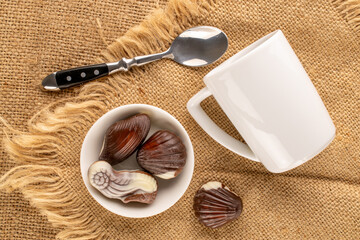 Several chocolate candies with ceramic dishes on jute cloth, close-up, top view.