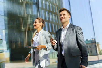 Business professionals walking outside modern office building while checking their devices in the afternoon