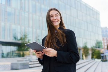 Young woman using tablet while standing outside a modern building in an urban setting