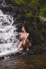 Fototapeta premium Mulher sentada sobre a rocha, numa cascata