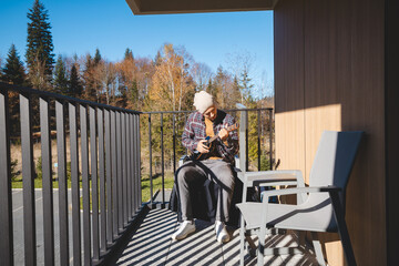 Young musician sits on a sunny balcony, immersed in playing the ukulele. Surrounded by autumn...
