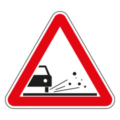 Red triangular road sign warning of loose road surface with gravel or chippings flying from under car wheels