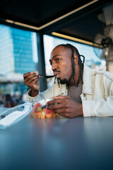 Young man enjoying a healthy fruit salad during lunch break in a modern city