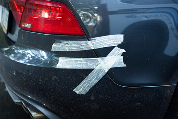Car bumper fixed with tape. Broken rear exterior of a dark car. Provisional repair after an accident. Slightly damaged automobile due to a crash.