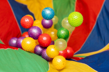 colorful plastic balls being shaken around in a striped children's parachute during a children's birthday party