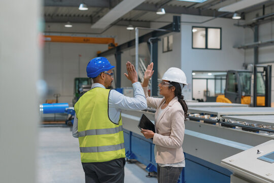 Female manager engineer giving high five to industry worker in manufacture factory.
