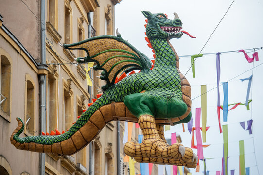 gros dragon vert et jaune, avec des ailes, qui crache du feu, monstre mythique suspendu sur un c&acirc;ble en haut de l'entr&eacute;e d'une rue