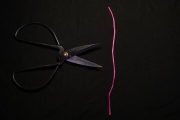 A pair of vintage-style metal scissors placed next to a pink ribbon, displayed on a black surface.