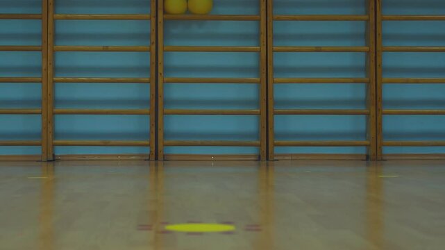 Wooden wall bars gradually closing against blue wall in empty fitness center, revealing minimalist sports hall interior with parquet flooring