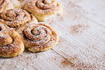 Freshly baked cinnamon rolls are arranged on a rustic wooden table, dusted with powdered sugar.