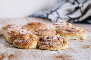 Homemade cinnamon rolls topped with powdered sugar rest on a rustic wooden kitchen table.