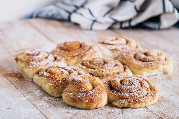 Warm, freshly baked cinnamon rolls with sugar dusting on a rustic wooden table in cozy setting.