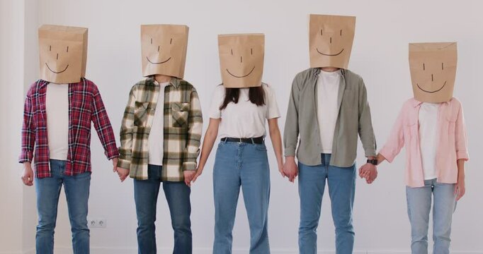 Row of people with paper bags on their heads with cheerful painted smiles nod in agreement together. Unknown men and women stand holding hands. Concept of unanimity, positivity and collective approval