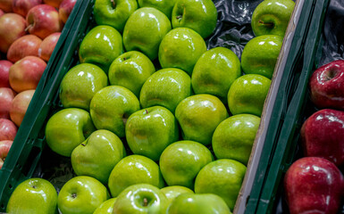 Fresh green apples in a neatly organized tray alongside red apples at a local market. Vibrant and...