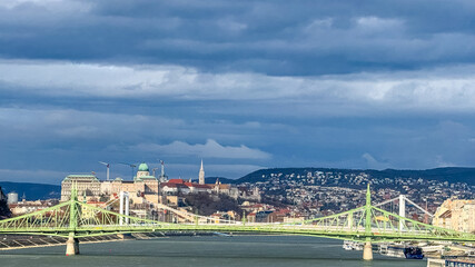 A panoramic view of Budapest's Liberty Bridge and Buda Castle under dramatic clouds, ideal for travel and tourism themes