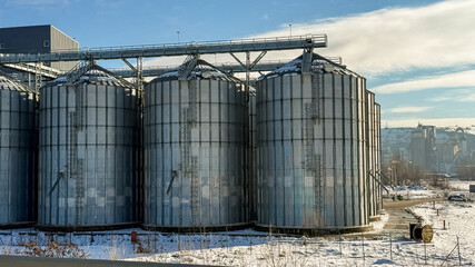 A row of large grain silos in a snowy landscape represents agricultural storage solutions during...