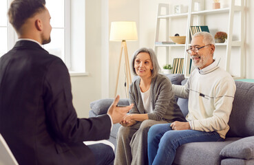 Gray-haired happy smiling senior couple sitting on sofa in the living room at home and having...