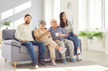 Happy family at home, senior old parents and adult children sitting on sofa together, laughing,...
