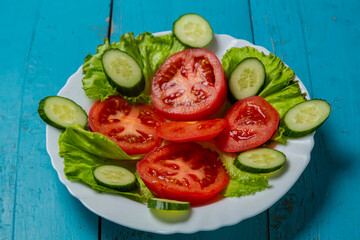 Salad, cucumbers and tomatoes in circles in a white plate on a blue wooden table