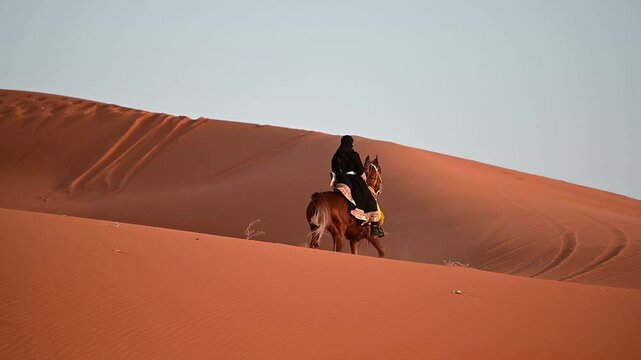 A Saudi woman, dressed in traditional attire, rides gracefully on a horse through the vast desert of Saudi Arabia. The golden sands stretch endlessly, with her figure embodying strength and culture