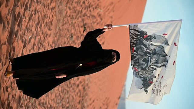 In the desert, a Saudi woman in elegant traditional attire celebrates Founding and national day with pride, embodying heritage, Waving founding flag. Vertical video