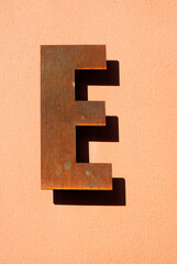Iron rusty letter E with shadow hanging on a ochre wall