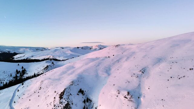 Aerial ascending drone view of mountains landscape at sunset in the winter season. Hills covered by snow in Bucegi natural park, Romania