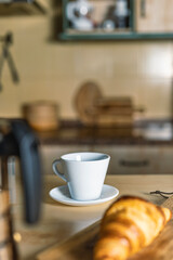 Breakfast in the kitchen with freshly made croissant and hot cup of coffee. Coffee maker, croissant and kitchen out of focus
