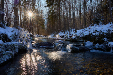 Landschaftsfoto. Winterlicher Bach mit Sonnenstern am Himmel. Bei kalten Temperaturen.