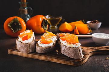 Sandwiches on rye ciabatta with ricotta, persimmon, honey and nuts on a board on a table