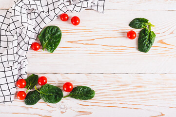 Spinach leaves, cherry tomatoes and fabric on white wooden background top view