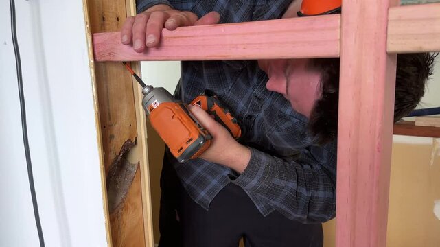 A man drilling diagonally upwards from underneath into the nogging to secure it to the stud where the fastener is driven at an angle to create a solid joint between the perpendicular timbers